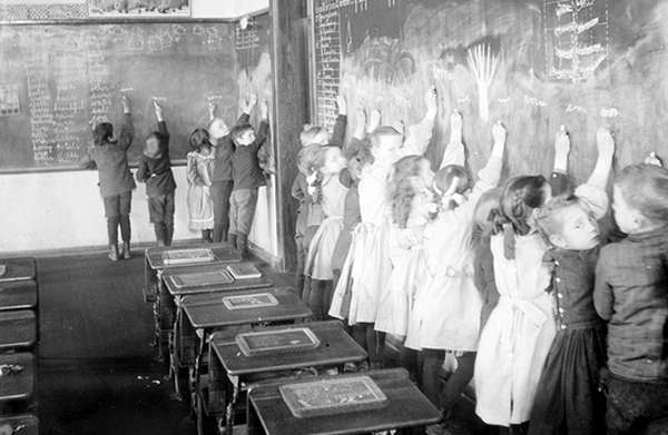 Aula de una escuela con niños escribiendo en la pizarra.